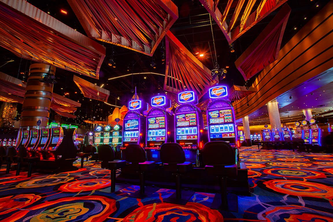 Fila de máquinas tragamonedas con carteles de jackpot iluminados en morado y naranja